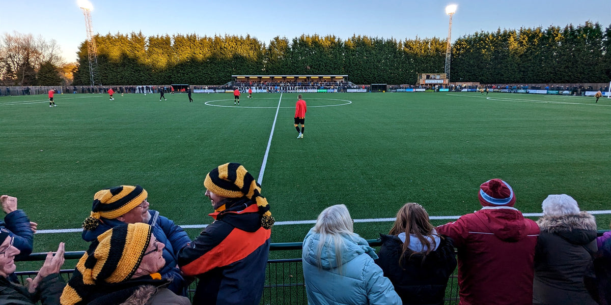 Supporters watching from behind the barrier, floodlit pitch beyond